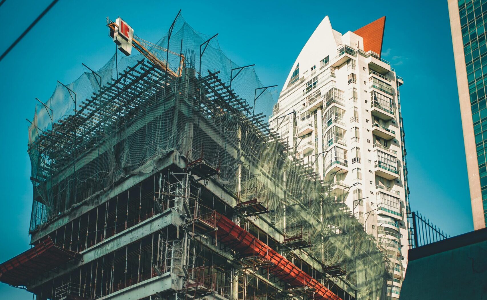 High-rise building under construction with scaffolding and crane in urban cityscape.